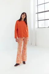 Pantalon de corte acampanado con diseño estampado geométrico en tonos naranjas, blancos y rosados.