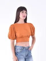 Blusa corta color naranja, con mangas abullonadas y puños elásticos. Presenta un diseño ajustado en la cintura y escote redondo.