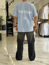 Remera oversize de efecto gastado color celeste, con cuello redondo y mangas cortas. Estampado frontal pequeño con el texto "Top Style" y gran estampado en la espalda con el mismo texto, la frase "Dream big. Work hard. Make it real.", el año "SINCE 2021" y un código de barras.