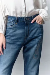 Jean de corte recto y tiro alto confeccionado en denim azul rígido. Presenta un diseño de hotfix brillante aplicado sobre la superficie del pantalón. Cuenta con cierre y botón frontal.