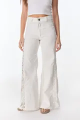 Pantalón de jean negro de pierna ancha con cortes laterales y godets triangulares en tela de broderie o encaje color crudo para mayor amplitud.