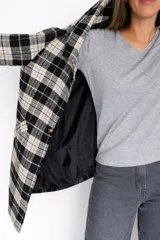 Chaqueta larga de corte recto con estampado de cuadros en tonos marrones y beige. Presenta cuello con solapas, cierre frontal con un botón y bolsillos laterales funcionales. Incluye forro interior.