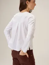 Remera de manga larga color blanco con costuras decorativas en contraste y una franja lateral oscura a lo largo de las mangas. Presenta un diseño de cuello redondo y corte holgado.