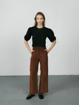 Pantalón de corte recto y tiro alto, confeccionado en pana color marrón, con bolsillos laterales y cierre frontal con botón y cremallera.