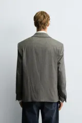 Blazer de corte boxy fit con estampado de espiga. Presenta cuello con solapas de muesca, cierre frontal de un botón, mangas largas con puños abotonados y bolsillos con solapa en la cadera.