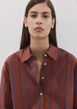 Blusa de algodón marrón con rayas verticales azules, corte recto, cuello camisero, manga larga con puños abotonados y cierre frontal de botones.