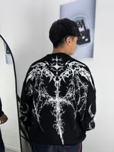 Sweater de tejido de punto en color negro con un diseño gráfico grande y detallado en blanco en la espalda, que presenta motivos abstractos y góticos. Tiene cuello redondo y mangas largas con diseño holgado.