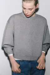 Sudadera gris de cuello redondo y manga larga, con puños y dobladillo acanalados.