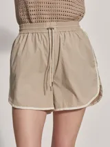 Short deportivo color beige con ribetes blancos, cintura elastizada y corte holgado.