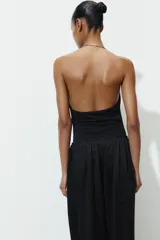 Body negro de cuello halter con detalle de pieza metálica y aplicación joya. Escote pico pronunciado y tejido drapeado. Cierre en bajo con botones a presión.