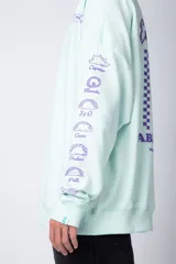 Buzo oversize de cuello redondo en color verde menta, confeccionado en tela rústica. Presenta un pequeño estampado en el pecho y una serie de estampados verticales a lo largo de la manga izquierda.