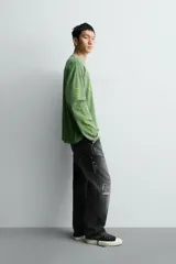 Camiseta de manga larga con corte relajado y cuello redondo, confeccionada con un acabado de efecto lavado. Presenta un estampado frontal con tipografía gótica y números en contraste.