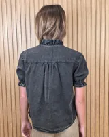 Camisa de denim de algodón celeste, con cierre frontal de botones, cuello alto con volados y mangas cortas abullonadas con puños elastizados fruncidos.