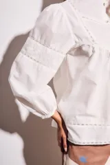 Blusa blanca de algodón con cuello mao, mangas largas abullonadas y detalles de encaje en el canesú, mangas y ruedo. Cierre frontal con botones.
