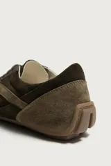 Zapatilla de cordones confeccionada en piel con acabado de serraje en tonos marrones. Presenta un diseño de perfil bajo con suela ultrafina a contraste y detalle de pespuntes decorativos.