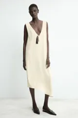 Vestido midi de color beige con diseño jacquard sutil. Presenta un escote en pico pronunciado, tirantes anchos y un bajo con acabado asimétrico.