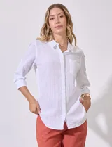 Camisa blanca de corte clásico con textura de líneas verticales, cuello con solapa, cierre frontal con botones y bolsillo en el pecho. Presenta mangas tres cuartos regulables con presilla y botón.