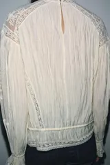 Blusa color crema de algodón con cuello alto, manga larga y bordados florales.