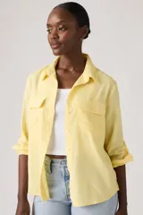 Camisa de lino color amarillo pastel, con bolsillos frontales con solapa, mangas largas remangadas y cierre frontal con botones.
