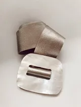 Faja ancha color dorado con hebilla rectangular de nácar. La hebilla presenta una abertura rectangular central. El cuero es intercambiable y se puede elegir el color.
