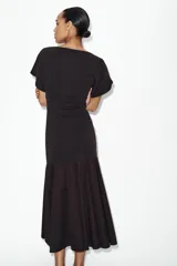 Vestido midi de color negro, confeccionado en tejido de punto con cuello barco y manga corta. Presenta un diseño ajustado en el torso que se combina con una falda inferior con vuelo y acabado evasé.