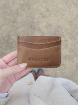 Tarjetero compacto de cuero marrón con ranuras para tarjetas y el logo de la marca grabado en la parte frontal.
