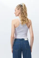 Top de algodón blanco sin mangas con cuello halter y bajo asimétrico en punta diagonal. Presenta un tejido de punto acanalado y un diseño inspirado en la estética de los años 2000.