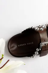 Sandalias marrones de cuero con doble tira, hebillas plateadas y apliques de tachas redondas plateadas.