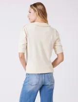 Buzo tejido color beige, marca Nanette, con cuello a la base y solapa decorada con apliques de perlas. Tiene manga corta con puño y ruedo acanalado.