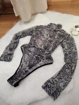 Body de manga larga y cuello alto, confeccionado en microtul estampado con diseño animal print abstracto. Presenta una espalda descubierta y cierre con broches en la entrepierna.