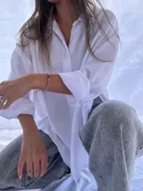 Camisa blanca de corte oversize, con cuello clásico, cierre frontal de botones y mangas largas con puños abotonados.