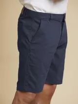 Bermuda de gabardina azul marino con bolsillos laterales y traseros, cierre frontal con botón y cremallera, y trabillas para cinturón.