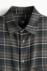 Camisa de manga larga con ajuste relajado, cuello inglés y un bolsillo de parche en el pecho. Presenta un estampado de cuadros en tonos de verde militar y negro, con finas líneas blancas.