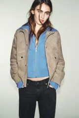 Cazadora de ante con cuello subido, manga larga y bajo elástico. Presenta cierre frontal con cremallera oculta y botones a presión, además de bolsillos delanteros con solapa.