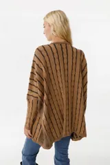 Sweater de punto color camel con diseño de trenzas verticales y acabado brillante. Presenta una silueta holgada tipo poncho, cuello redondo, mangas largas con puños ajustados y bolsillos frontales con detalle de etiqueta de cuero.
