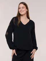Blusa azul de corte holgado y fluido, con escote en V y mangas largas raglán que presentan detalles de calados con forma de flores y puños elastizados.