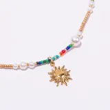 Collar tipo gargantilla con cadena dorada ajustable, intercalada con cuentas de semillas multicolores y perlas blancas. Incluye un dije colgante dorado con forma de sol radiante.