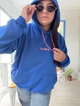 Canguro deportivo de tela suave con logo bordado, diseño holgado y mangas largas.