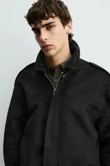 Cazadora cropped fit color verde militar, confeccionada en tejido efecto ante. Cuenta con cuello solapa, manga larga con puño abotonado, trabillas en los hombros, bolsillos laterales ocultos y un bolsillo interior. El bajo tiene elástico interior y el cierre frontal es con cremallera oculta por solapa con botones a presión.