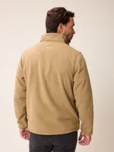 Campera de polar color beige con cierre frontal completo y cuello alto. Presenta un bolsillo en el pecho con cierre y detalle de parche con logo. El diseño combina paneles de tejido polar con detalles en tejido técnico en la zona del pecho.