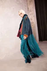 Tapado artesanal tejido en telar con lana teñida, presenta solapas y detalles en cuero natural con terminaciones de pasamanería. Diseño de corte amplio y textura tejida.