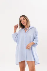 Vestido camisero de lino color celeste, con escote en V, cuello clásico, cierre frontal de botones y mangas tres cuartos regulables. Diseño holgado con corte asimétrico.