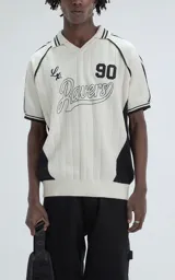Chomba de punto estilo deportivo, color blanco con detalles en negro. Presenta cuello polo con rayas, mangas cortas con franjas laterales, y diseño frontal con el número 90 y la palabra Ravers bordada.