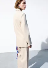 Blazer Paola de corte recto, color beige, confeccionado en mezcla de lana y lino. Presenta cuello pico con solapa, mangas largas, un bolsillo de ribete en el pecho, dos bolsillos con solapa en los laterales y cierre frontal de un botón oscuro.