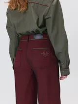 Pantalón sastrero de tiro medio, pierna ancha y corte recto, color bordó con finas rayas verticales y detalles de vivos a contratono en la pretina y el frente.