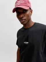 Remera negra de manga corta con cuello redondo y calce relajado, confeccionada en jersey de algodón orgánico. Presenta un pequeño estampado tipográfico en el centro del pecho con el texto 'JJ Studios'.