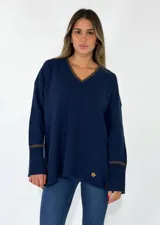 Sweater de punto azul marino con cuello en V, mangas largas con puños acanalados y detalle de línea en color marrón en el cuello y puños. Presenta un pequeño aplique decorativo en la parte inferior.