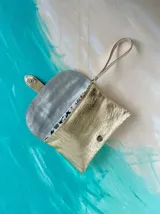 Sobre de mano Carolina De Cunto modelo Saria, confeccionado en cuero dorado brillante con textura y solapa plateada con detalles pintados a mano. Cuenta con tira de muñeca y cierre con broche imán.