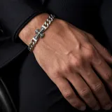 Pulsera de eslabones gruesos de acero con dije central en forma de cruz con detalles grabados.