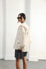 Camisa oversize de algodón color crema con rayas texturizadas, hombro caído y silueta amplia. Presenta un recorte delantero con vivo contrastante en color marrón, botones frontales y logo bordado en el frente.